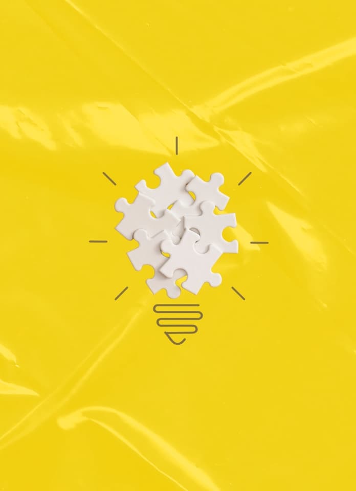 A lightbulb icon made of white puzzle pieces with simple line art rays and a base, on a bright yellow background.
