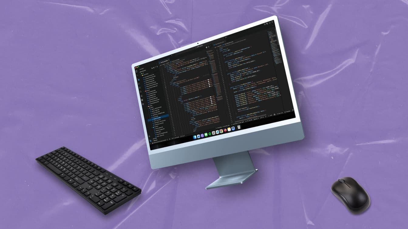Egy monitor programkóddal a képernyőjén, mellette egy fekete billentyűzet és egér lebeg lila fóliás háttér előtt.
