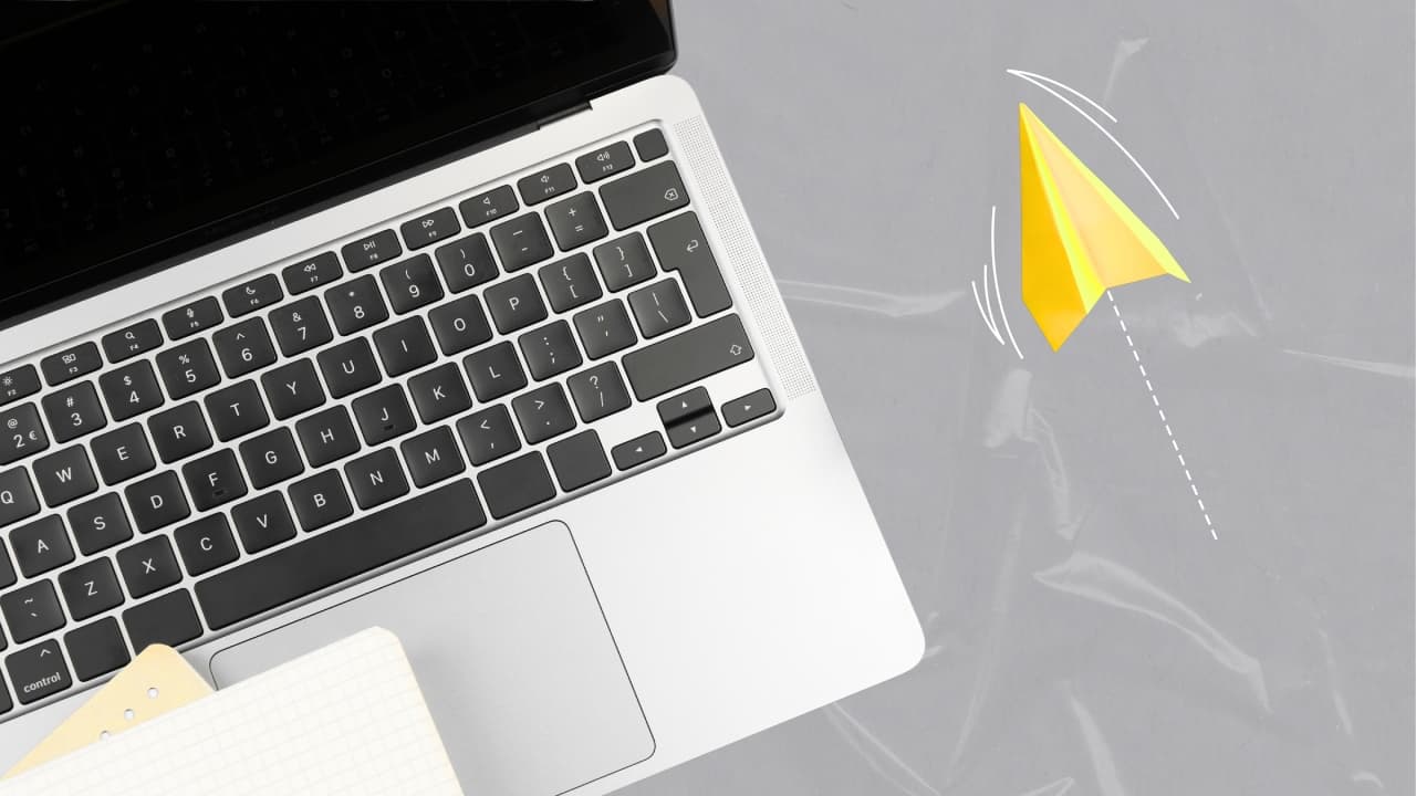 Laptop keyboard and yellow paper airplane on a gray background, illustrating website development and digital solutions.