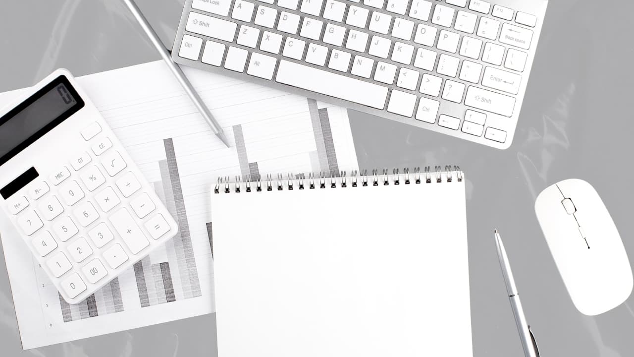 Weboldalkészítés és digitális tervezés: billentyűzet, egér, számológép, jegyzetfüzet és grafikonok egy szürke íróasztalon.