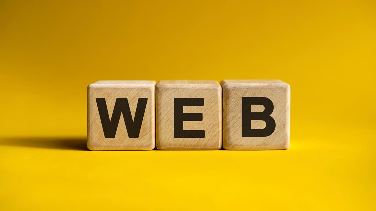 Három darab világosbarna fából készült kocka élénksárga háttér előtt, amelyeken a fekete "WEB" felirat olvasható.