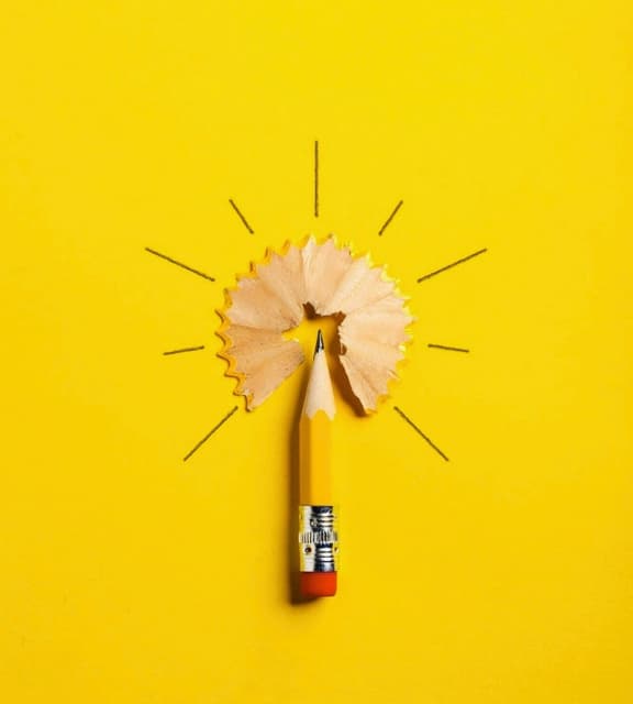 Yellow pencil with a shaving resembling a glowing lightbulb on a yellow background, symbolizing creativity.