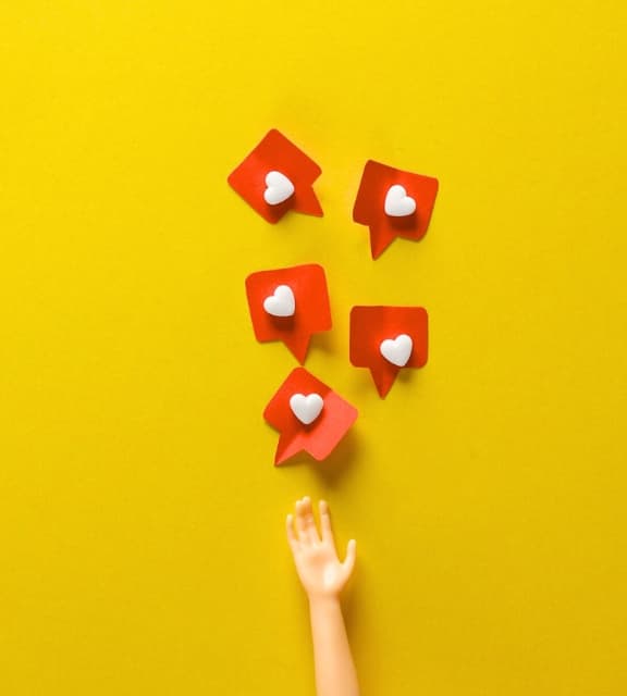 A doll's hand reaching up toward five red social media notification bubbles with white hearts on a yellow background.