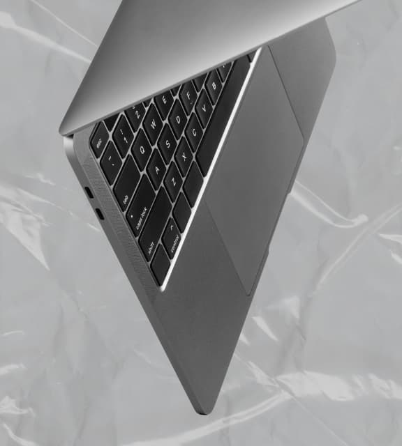 A sleek grey laptop captured from a dynamic angled view, resting on a crinkled grey plastic surface.
